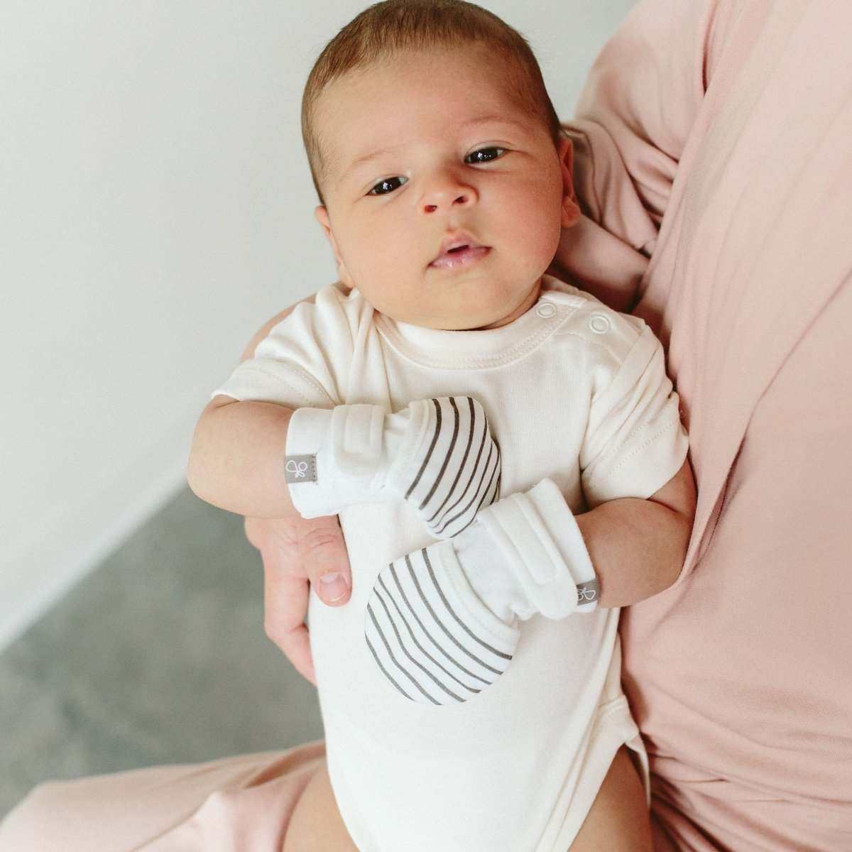 2-PACK MITTS baby mittens in soft white with thin gray stripes, worn as a pair with wide adjustable cuffs