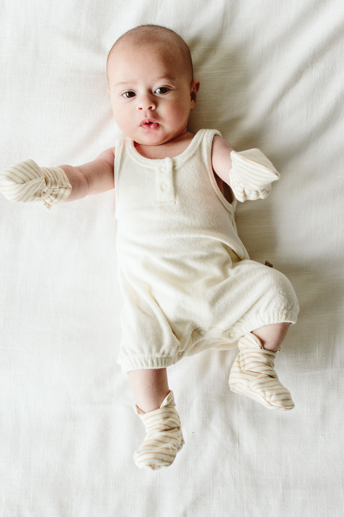 STAY ON 2-PACK BOOTS are soft cream baby booties with tan stripes and adjustable wrap closures, worn by a baby