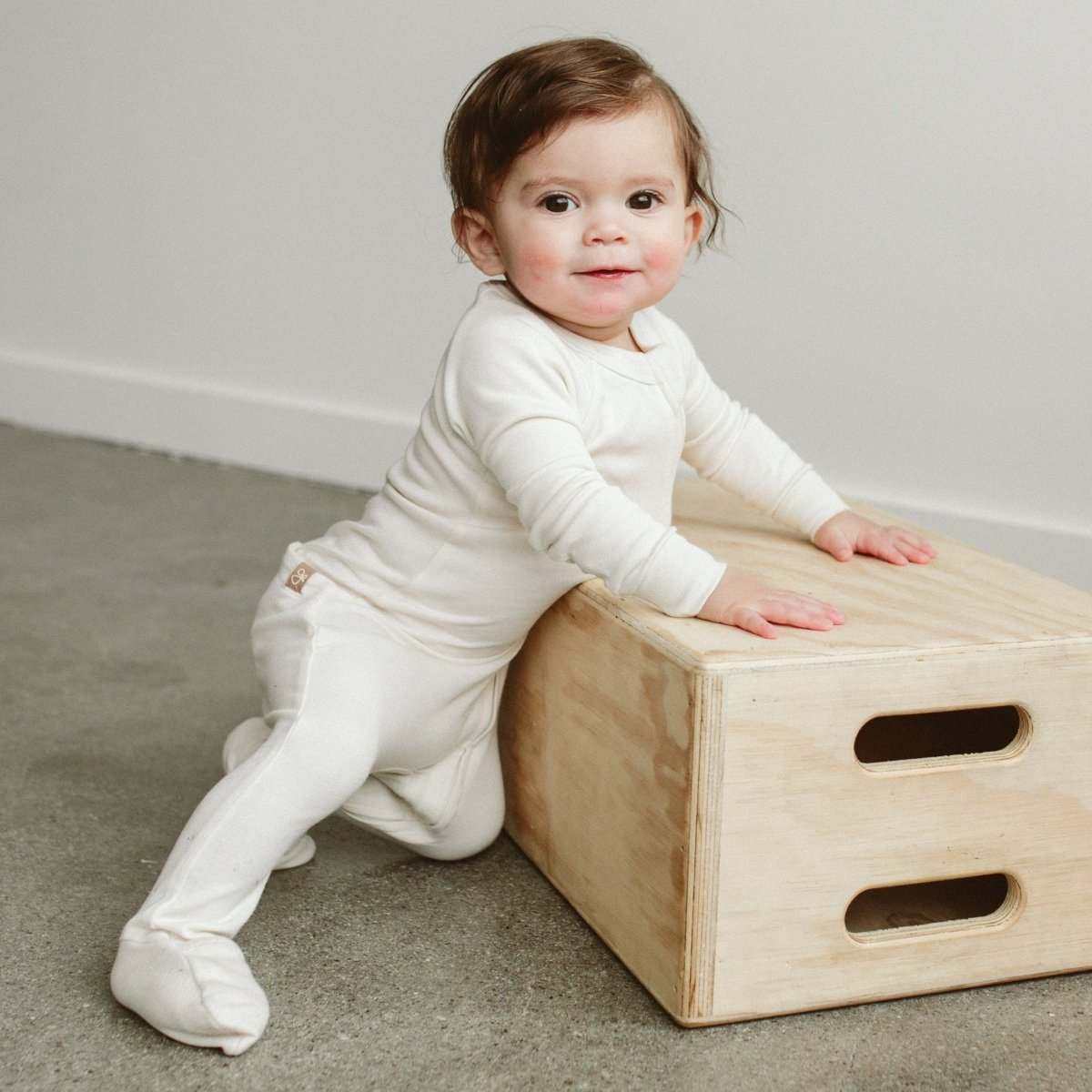 GROW WITH YOU FOOTIE in soft ivory fabric, worn by a baby, with long sleeves, covered feet and a convertible design