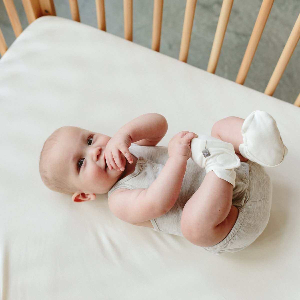 PREEMIE BOOTS in soft white fabric with an adjustable two-part closure, worn by a baby with a light grey outfit