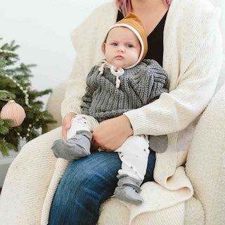 STAY ON 2-PACK BOOTS in soft grey knit with adjustable cuffs, worn by a baby with a mustard ribbed bonnet