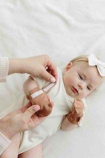 STAY ON 2-PACK MITTS in soft blush fabric, shown being fitted on a baby with a two-part adjustable closure.