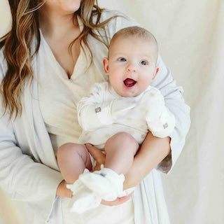 STAY ON 2-PACK MITTS are soft white baby mitts with adjustable cuffs, worn by a smiling baby.