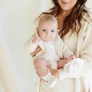 STAY ON 2-PACK MITTS in soft white fabric, shown on a baby with a wide cuff and adjustable closure
