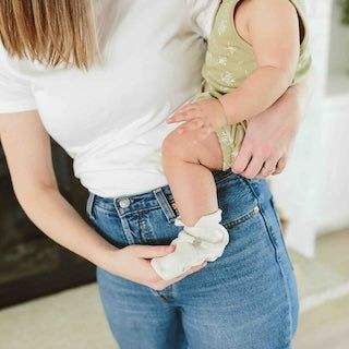 STAY ON BOOTS in soft white fabric with an adjustable wrap closure, worn on a baby’s foot