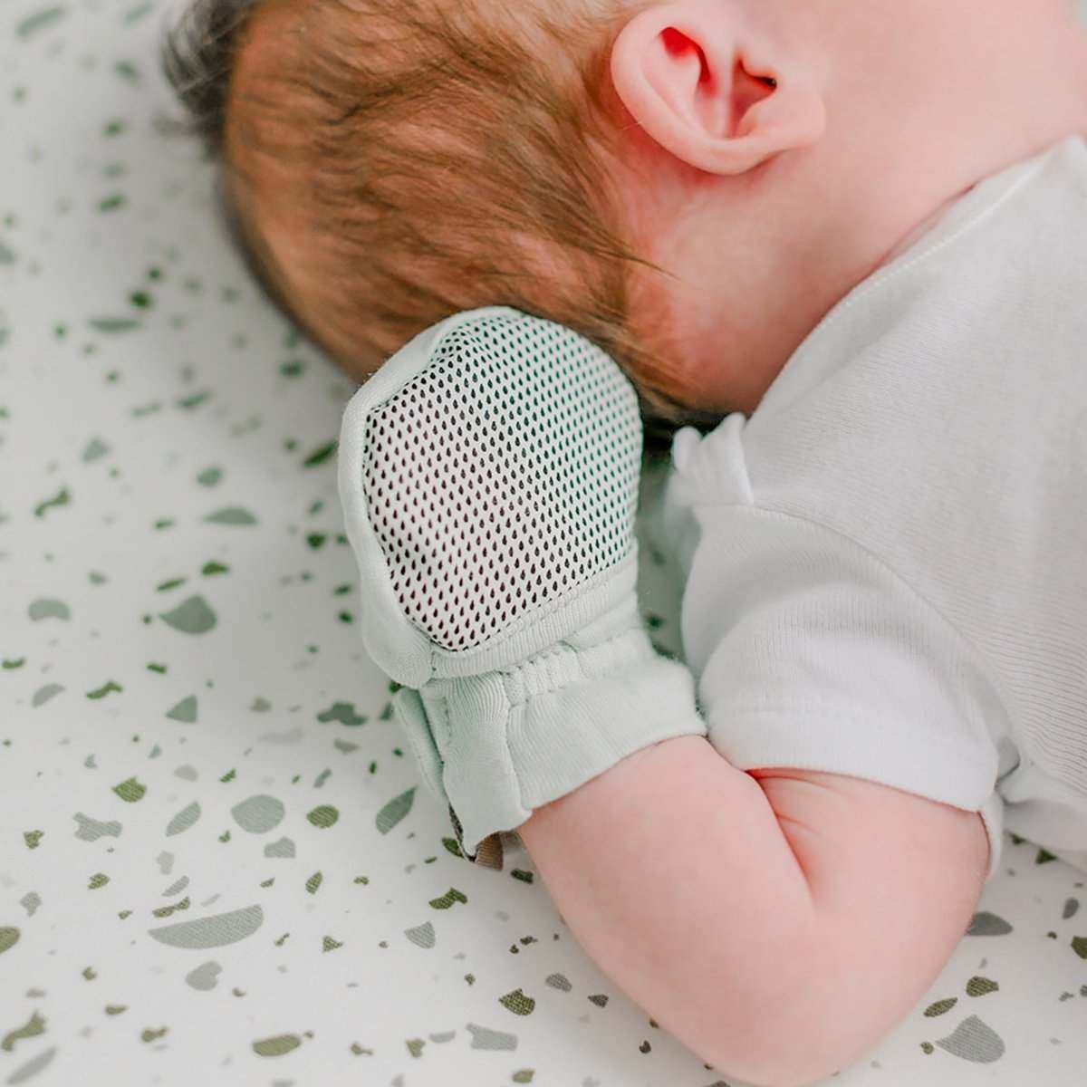 STAY ON MITTS: pale green baby mitt with a black and white dotted reversible panel and adjustable wrist closure