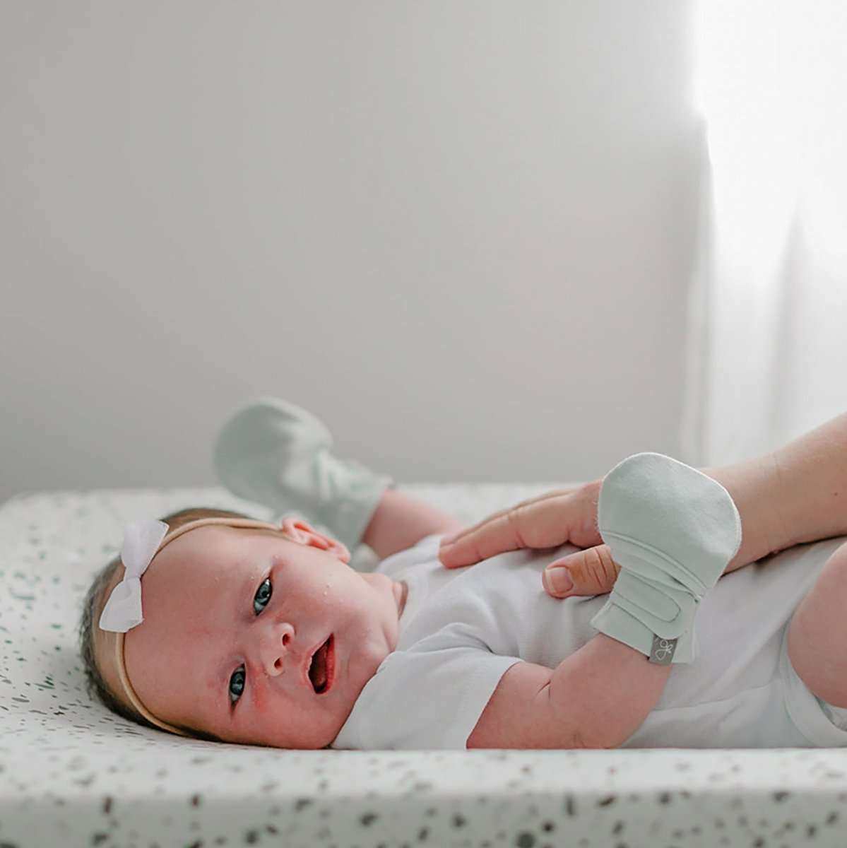 STAY ON MITTS in pale succulent green, soft fabric with an adjustable wraparound closure on a baby’s hands