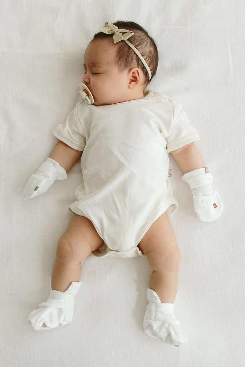 Stay on mitts in white with adjustable wrap closures, worn with matching soft white booties on a baby