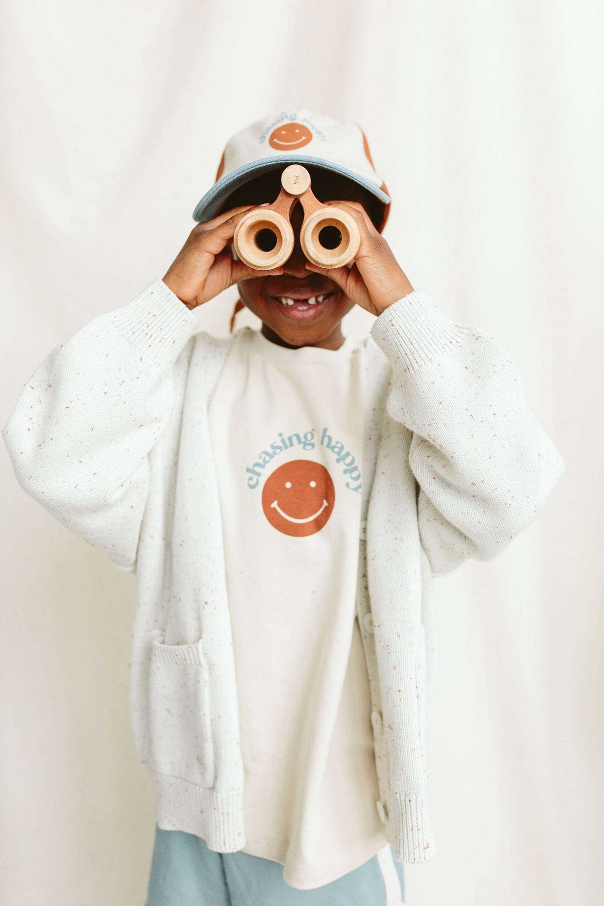 BALL CAP in light cream with an orange smiley face patch and dark brim, worn with a matching sweatshirt