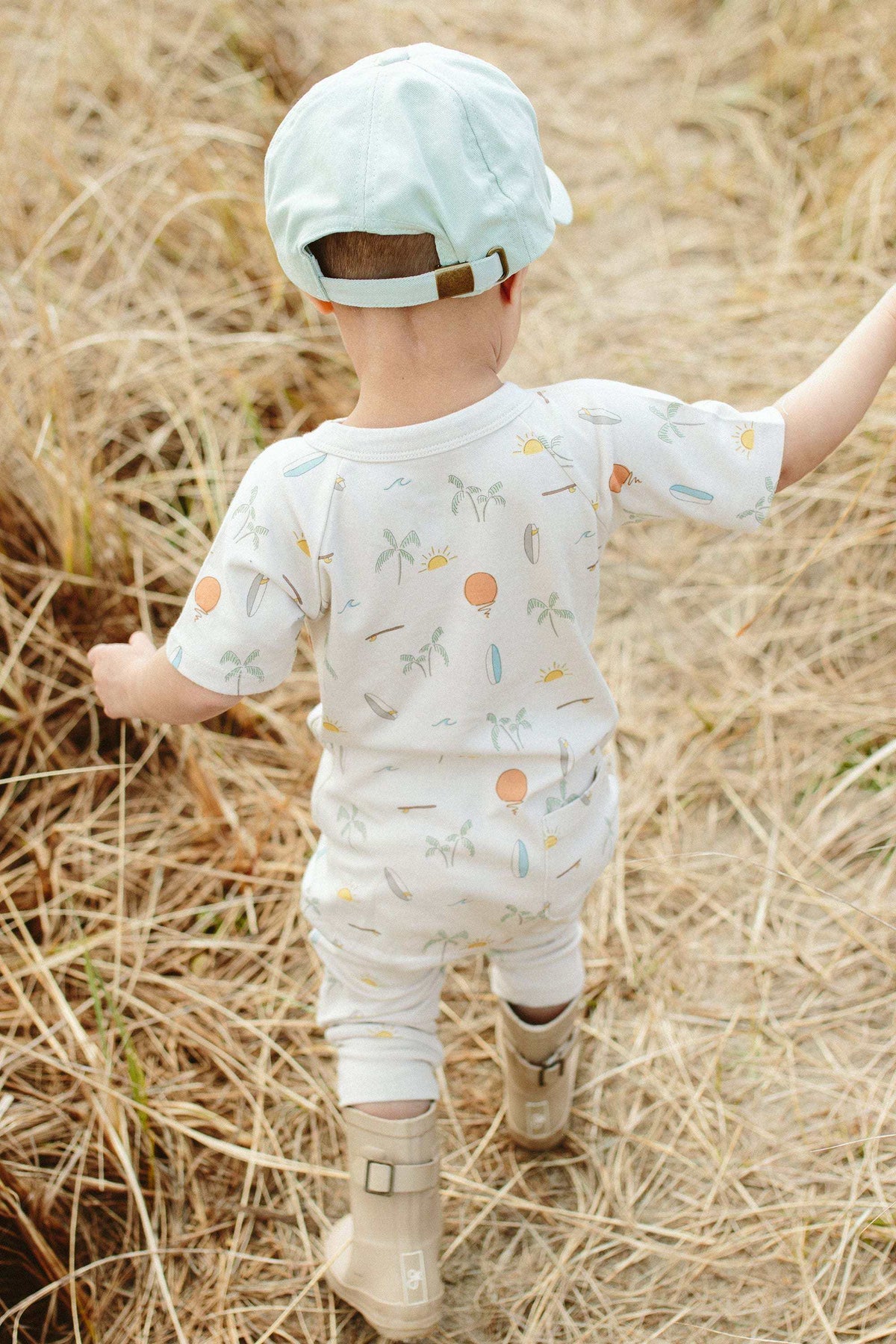 BALL CAP in pale aqua fabric with a curved brim and adjustable tan strap, worn backward by a child