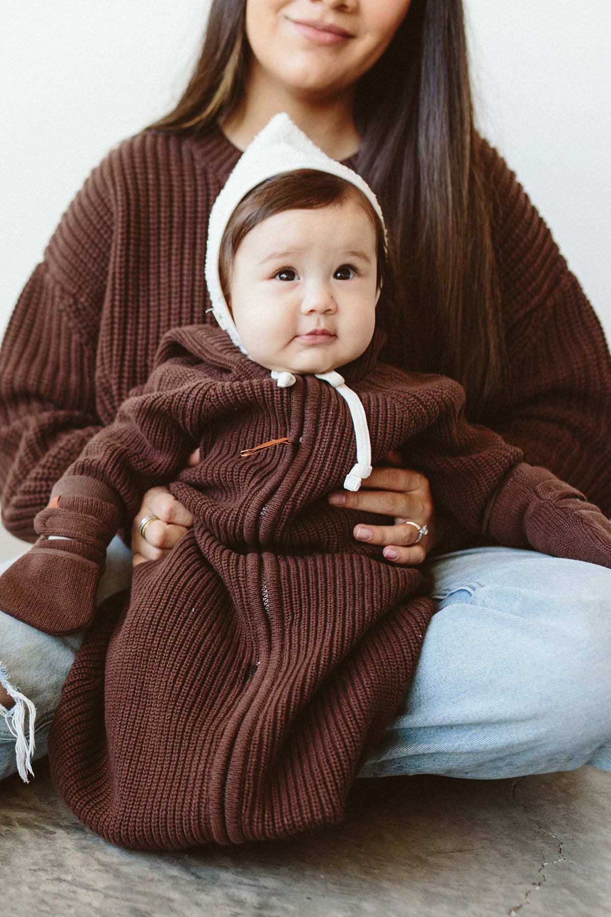 KNIT MITTS in dark brown ribbed knit with chunky cuffs and a small leather label, worn by a baby